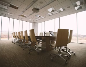 oficina con grandes ventanales, tonos beige y mesa de reuniones con sillas